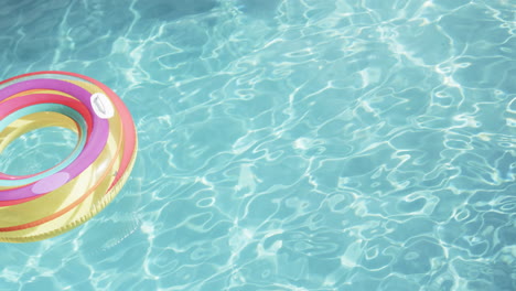 colourful inflatable ring floating in sunny swimming pool, copy space, slow motion