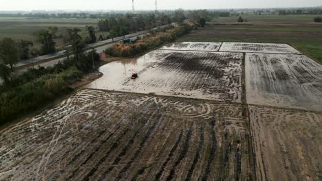 aerial view of a small tractor tilling a muddy rice paddy field