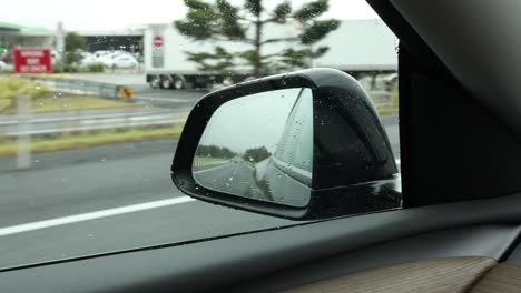 car's side mirror view of a rainy highway drive