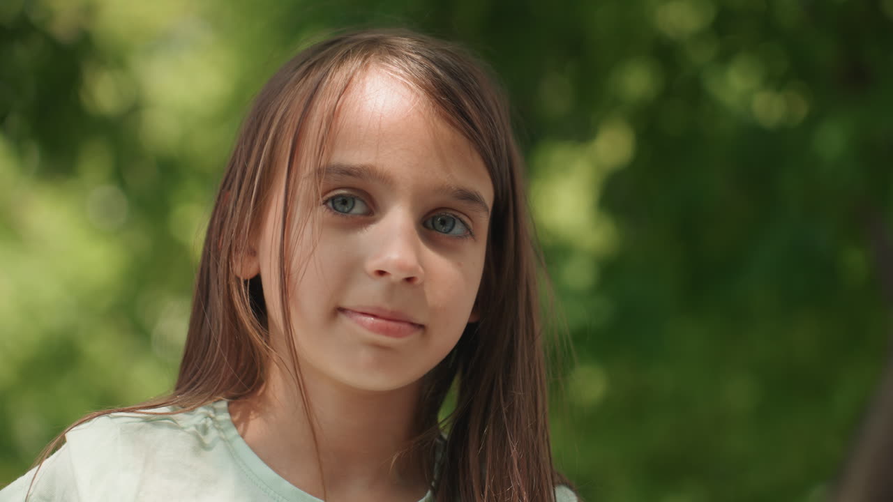 Filha pré-adolescente espiando através das árvores verdes, retrato de perfil com cabelo trançado e luz solar quente na pele, expressão pensativa e humor tranquilo, momento espontâneo ao ar livre ideal para a memória da família.