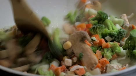 Cooking-and-mixing-frozen-vegetables-in-a-white-frying-pan,-making-healthy-vegetarian-food,-steam-coming-up,-closeup-handheld-shot