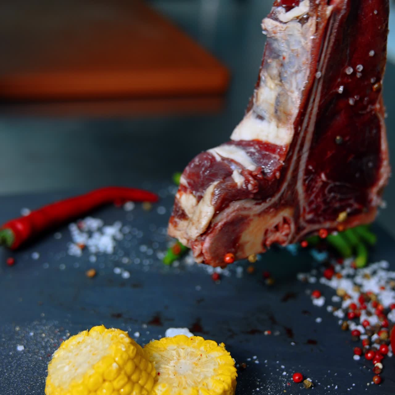 Una mano con guanti in lattice neri solleva un pezzo di carne da un tagliere. Coprendo la bistecca con sale e spezie. Primo piano. Sfondo sfocato. Schermo verticale.