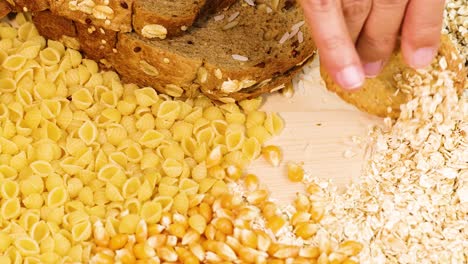 a hand organizes various grains and bread on a wooden surface under bright lighting, creating a visually appealing arrangement