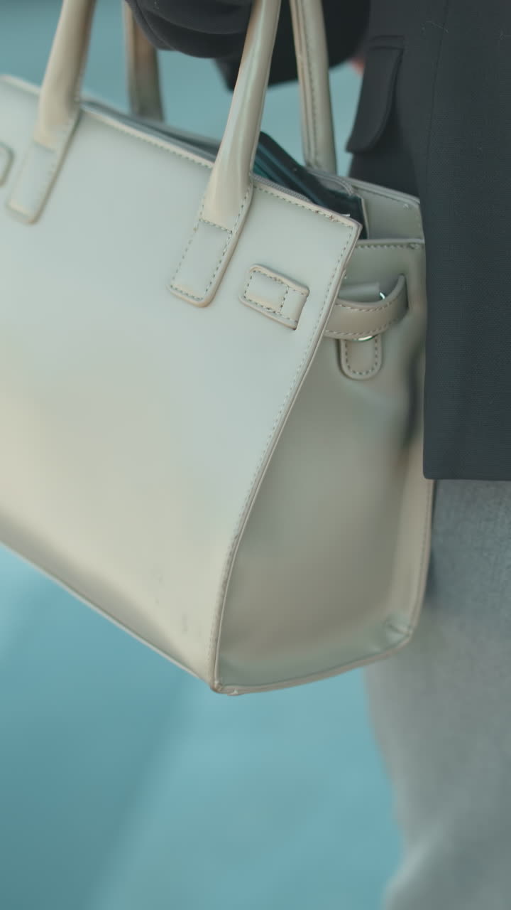 Primo piano da dietro di un docente in abbigliamento professionale che cammina con la borsa a mano al braccio, sfondo sfocato che mostra auto di passaggio e ambiente urbano