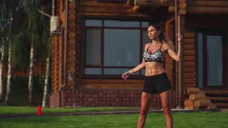 A-slim-and-beautiful-woman-in-sports-clothes-with-an-open-press-is-preparing-to-start-training-on-the-lawn-near-her-house-Performing-slopes-flexing-back-muscles