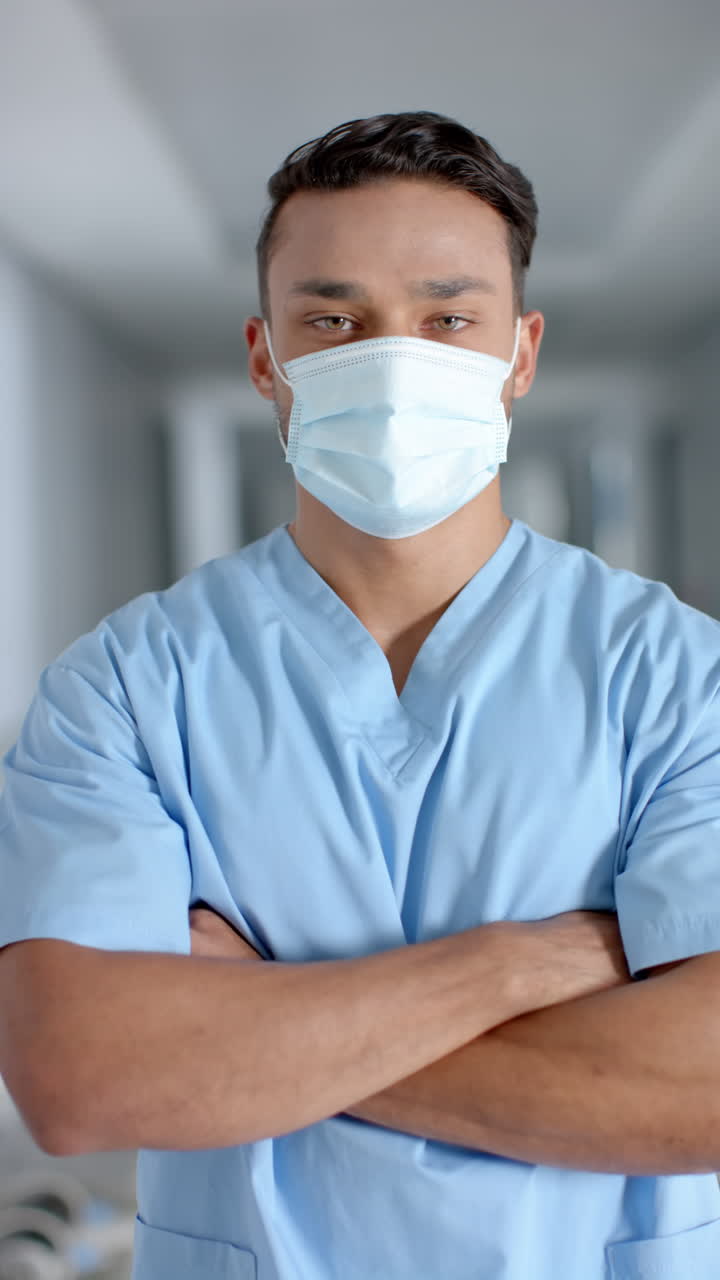 Vertical video of portrait of latino male doctor wearing face mask, slow motion