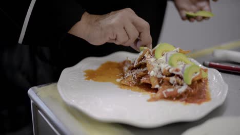 chef sou-chef cook preparing a traditional mexican dish called chilaquiles adding sliced avocado on top at a local cafe diner restaurant in latin america