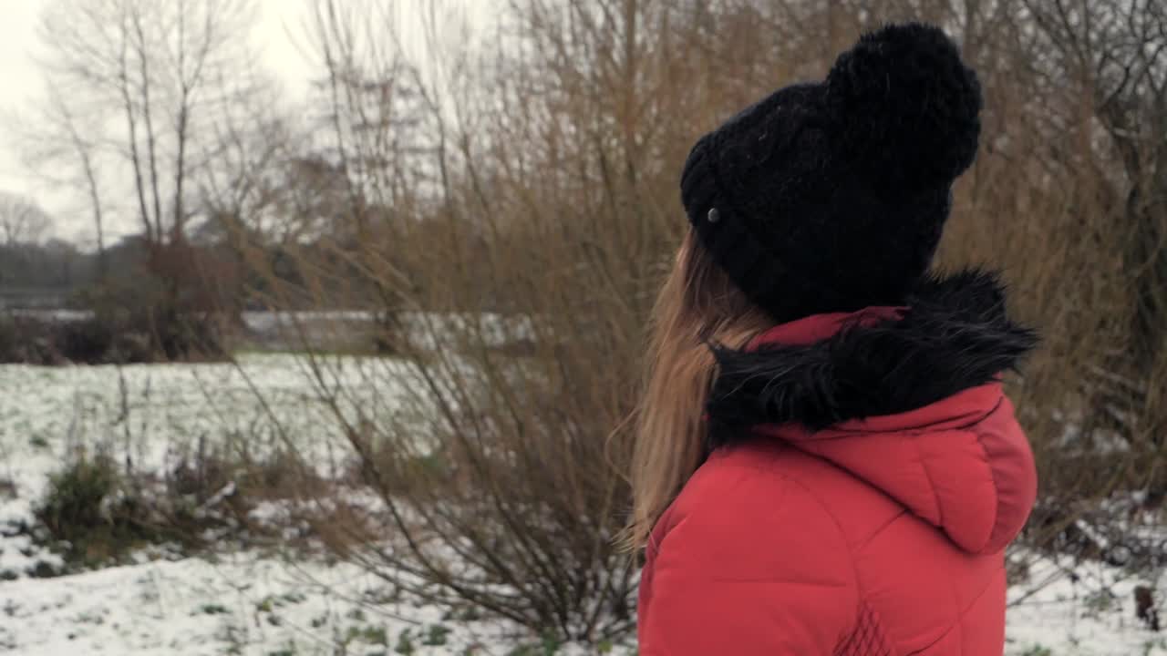 Girl in red coat walks slowly in winter landscape, captured in smooth slow motion.