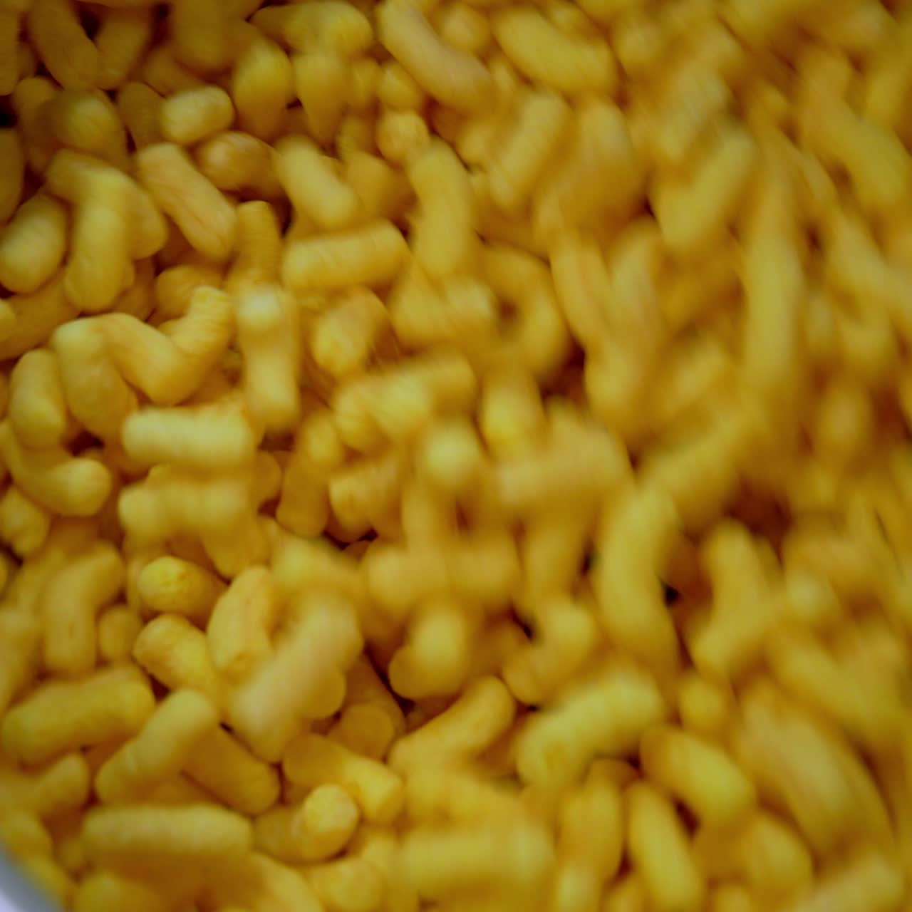 Tanti snack di mais dolce mescolati in un serbatoio di metallo. Primo piano. Produzione di bastoncini croccanti di mais in fabbrica.