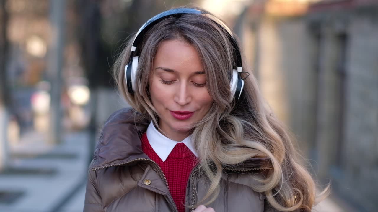 Woman listening to music in her headphones while singing along and dancing in the street