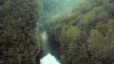 Langsame-Luftaufnahme,-Die-Träge-Einen-Nebligen,-Von-Bäumen-Gesäumten-Fluss-Hinuntertreibt,-Mit-Einer-Felswand-Auf-Der-Linken-Seite