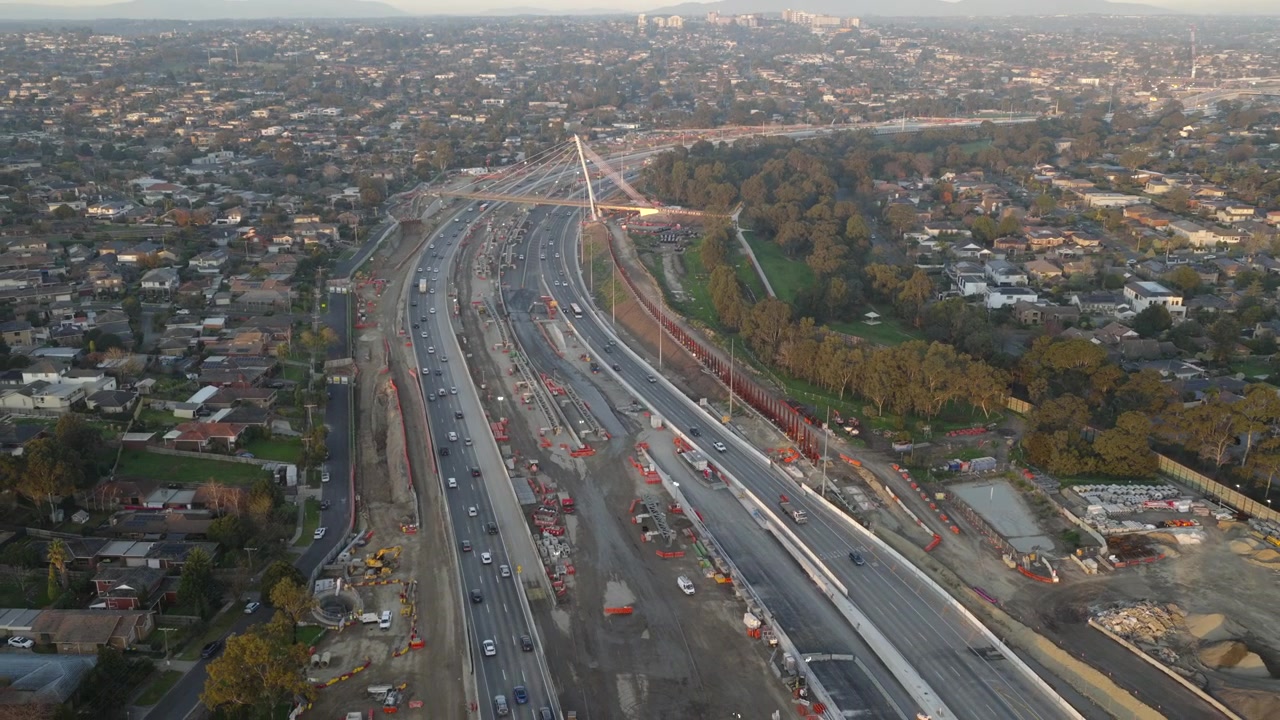 Aerial view of major EastLink freeway works in Doncaster, Melbourne, showing active traffic, expanded road corridors, construction zones and a cable-stayed bridge through suburban Melbourne.