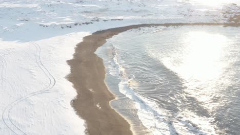 bright sunlight shines onto winter coastline of iceland with waves, aerial