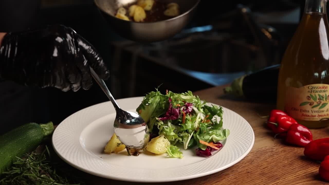 Chef Plating Roasted Potatoes and Fresh Salad in a Restaurant Kitchen