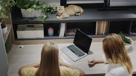 teacher or parent helping a girl who is working with a laptop in the classroom. top view