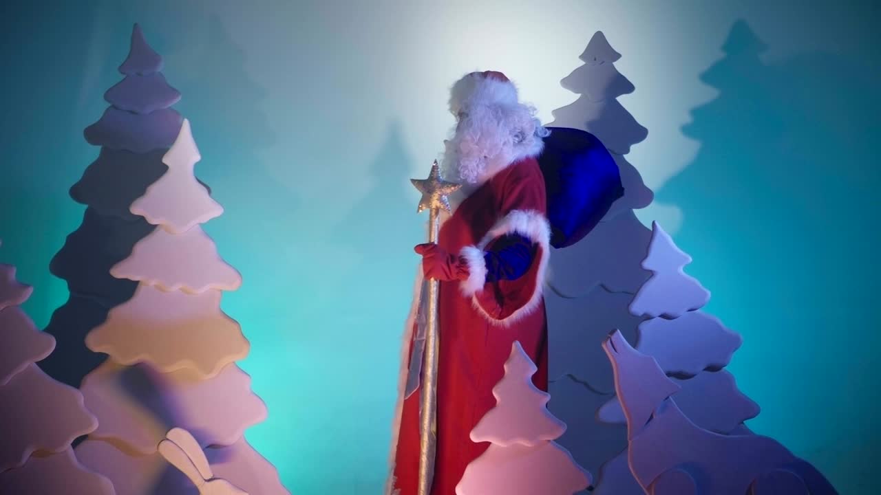 크리스마스 선물의 큰 가방을 가진 산타클로스는 동화 숲에서 산책하고 있습니다.