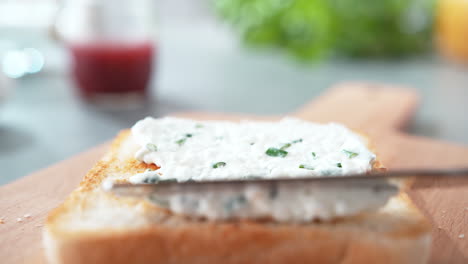 spreading cottage cheese with chives on lightly toasted bread with a table knife, breakfast in slow motion