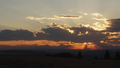 beautiful sunbeams peak through clouds rolling past a sunset at the edge of the alberta foothill; static shot 1080p