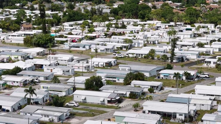 Una densa comunità di case mobili si estende a Bradenton, Florida, USA, mostrando file di tetti bianchi, palme, piccole piscine, strade strette sotto la luminosa luce del sole di mezzogiorno. Ampia inquadratura aerea con drone.