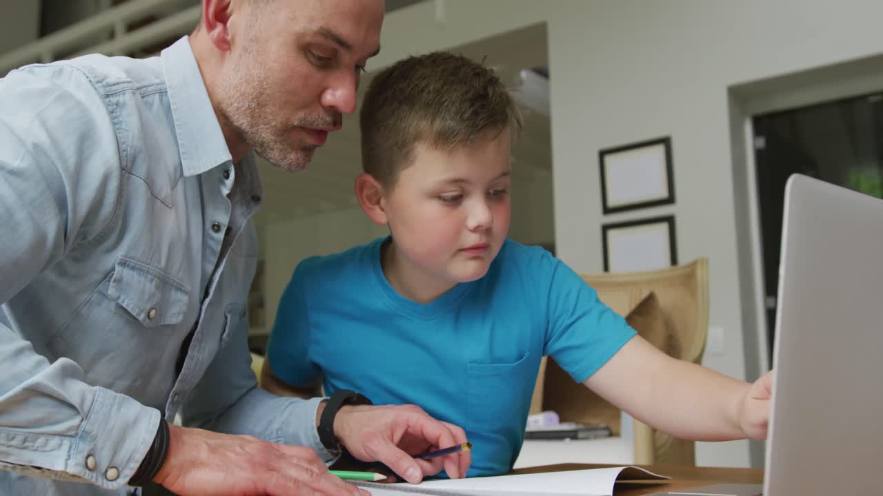 padre caucásico con su hijo sentado a la mesa y aprendiendo con una computadora portátil en casa