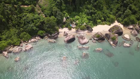 volando hacia el mar mientras vemos una pequeña playa con piedras gigantes de agua turquesa y la selva atlántica al fondo
