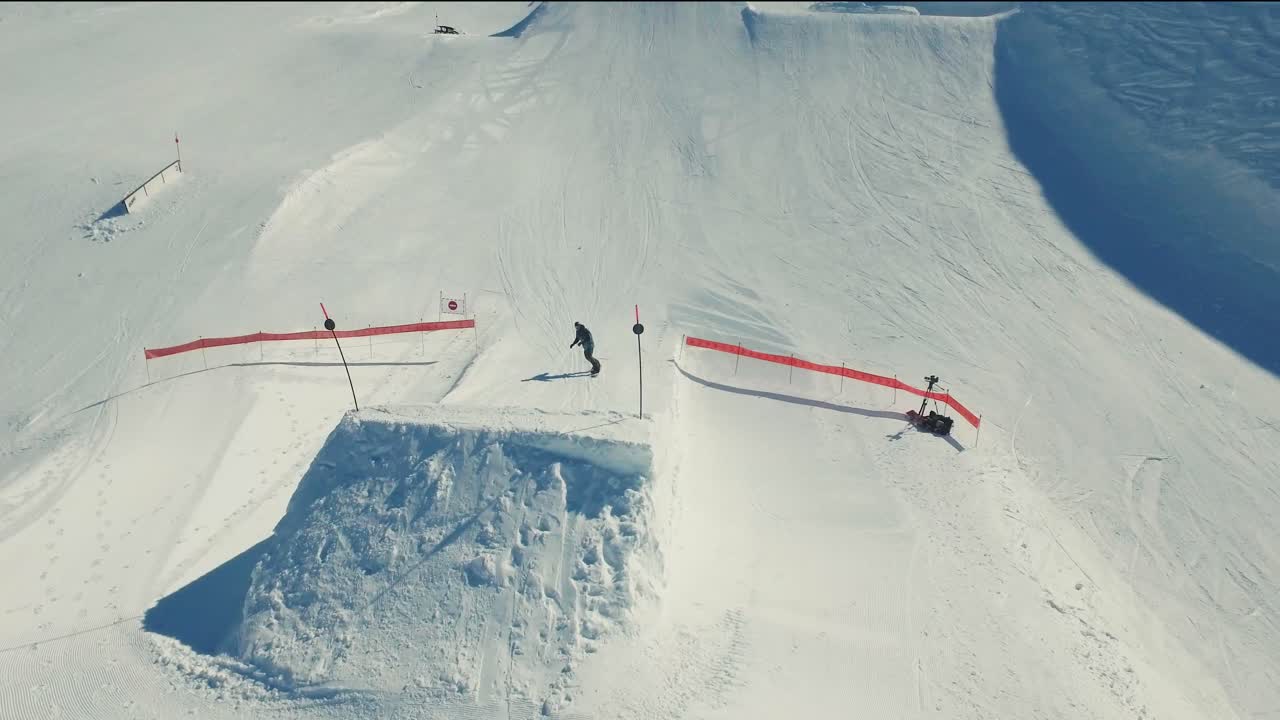 An aerial shot of a snowboarder going over a large kicker and doing a grab in the snowpark in Avoriaz, France