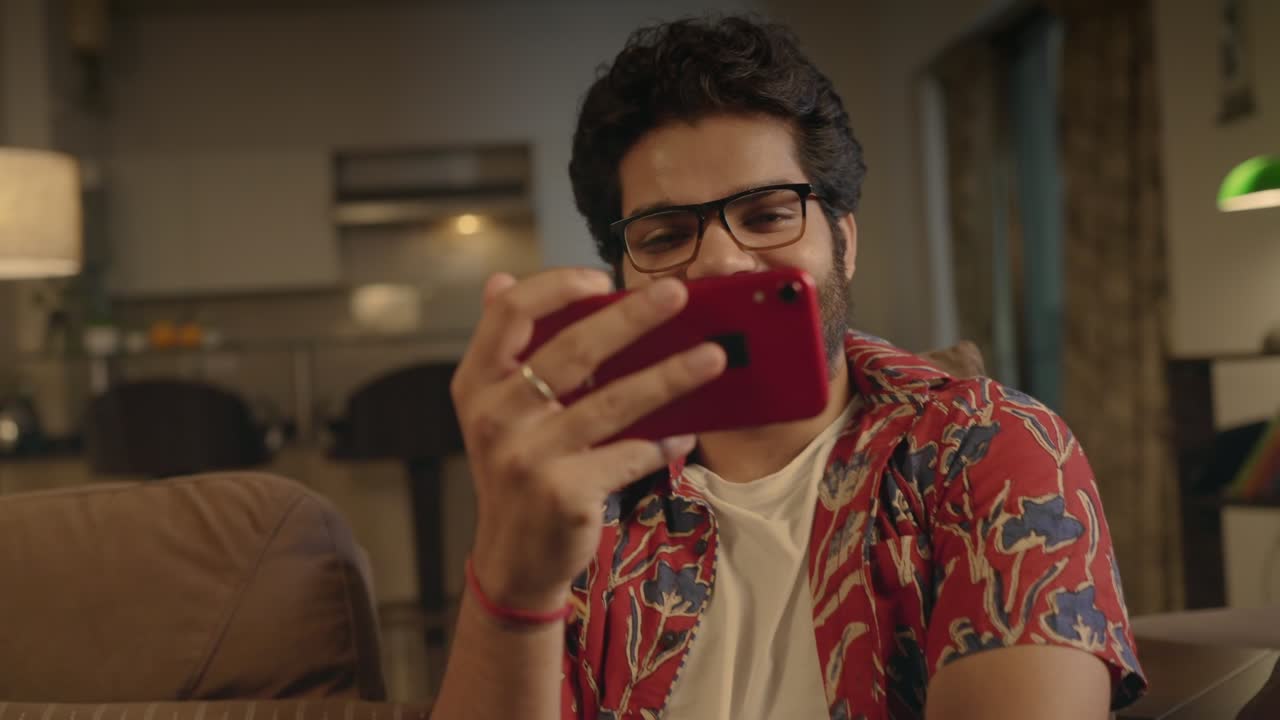 joven indio sentado en el sofá viendo una película en el teléfono móvil en casa