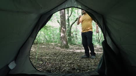 man stretching and preparing to go for a job in woodland area, view from inside tent on a bright day