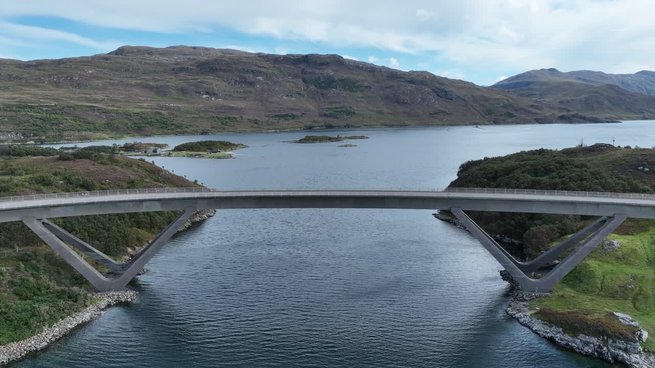Static aerial view of Laxford Bridge spanning a calm loch surrounded by rugged Highland mountains. Captured by drone on a clear day, showcasing Scotland’s natural beauty and modern road architecture