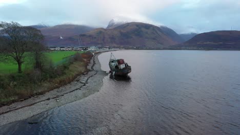 aerial footage slowly circling and then closing of the corpach shipwreck with ben nevis behind on a clear winter's day