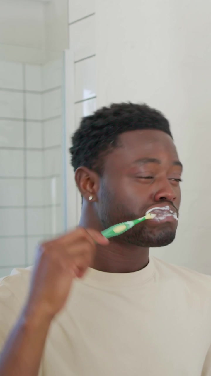 Vertical video: Bringing toothbrush, man in beige tee brushing teeth in bath mirror for oral care