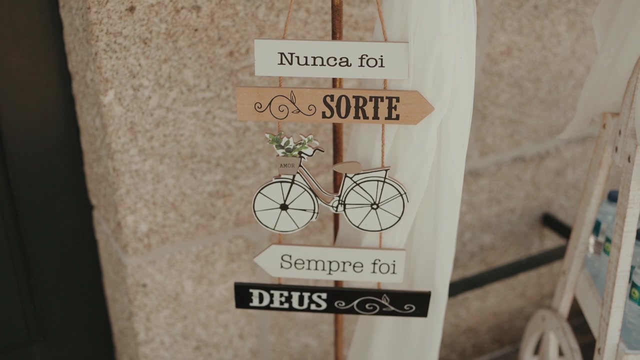 Lagdelt træskilt med portugisisk religiøst budskab og cykeludskæring hænger på en stenmur.