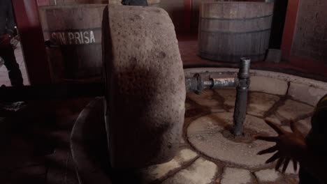 persona que explica el uso de una rueda de piedra en la producción artesanal de mezcal o tequila