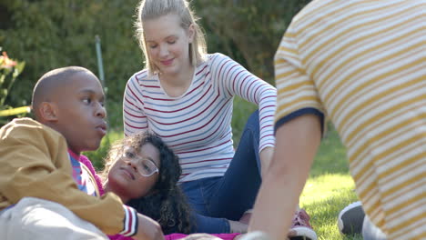 happy diverse group of teenage friends sitting on grass and talking in sunny park, slow motion