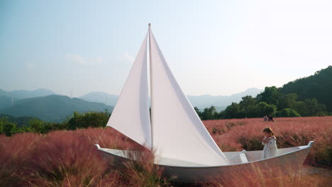 Kleines-Mädchen-Spielt-Seemann-In-Einem-Hölzernen-Segelboot-Auf-Dem-Rosafarbenen-Muhly-Grasfeld---Kräuterinselfarm-In-Pocheon