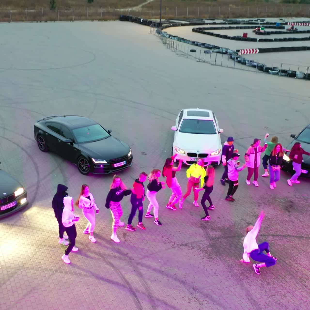 Dance group performing near the race cars. Young people take turns to dance in the middle. Top view. Karting at backdrop