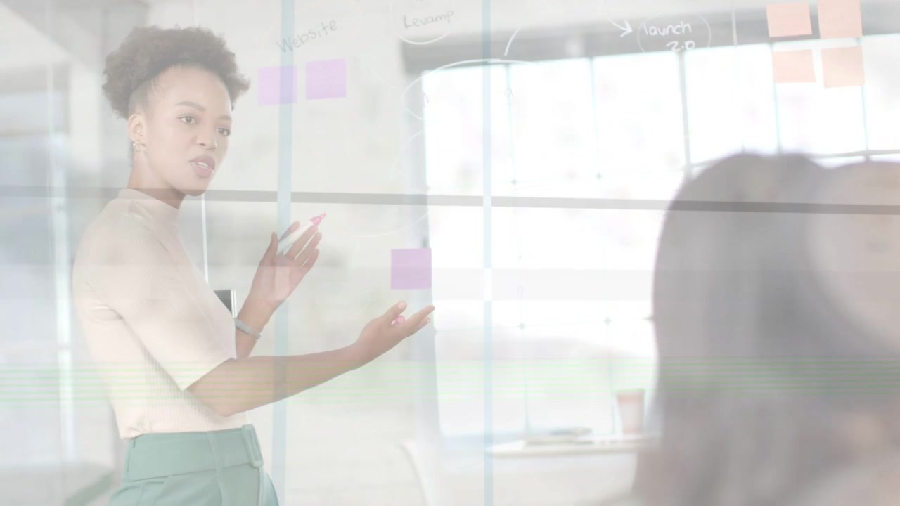 Woman turning to colleague and pointing at sticky notes on glass, presenting business ideas