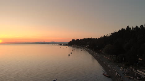 an-aerial-reveal-of-a-shoreline,-beach,-and-parked-boats-in-front-of-a-setting-sun