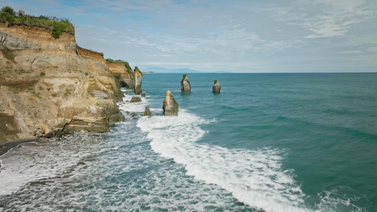 Waves breaking on coastal landscape with large sea stack columns, aerial