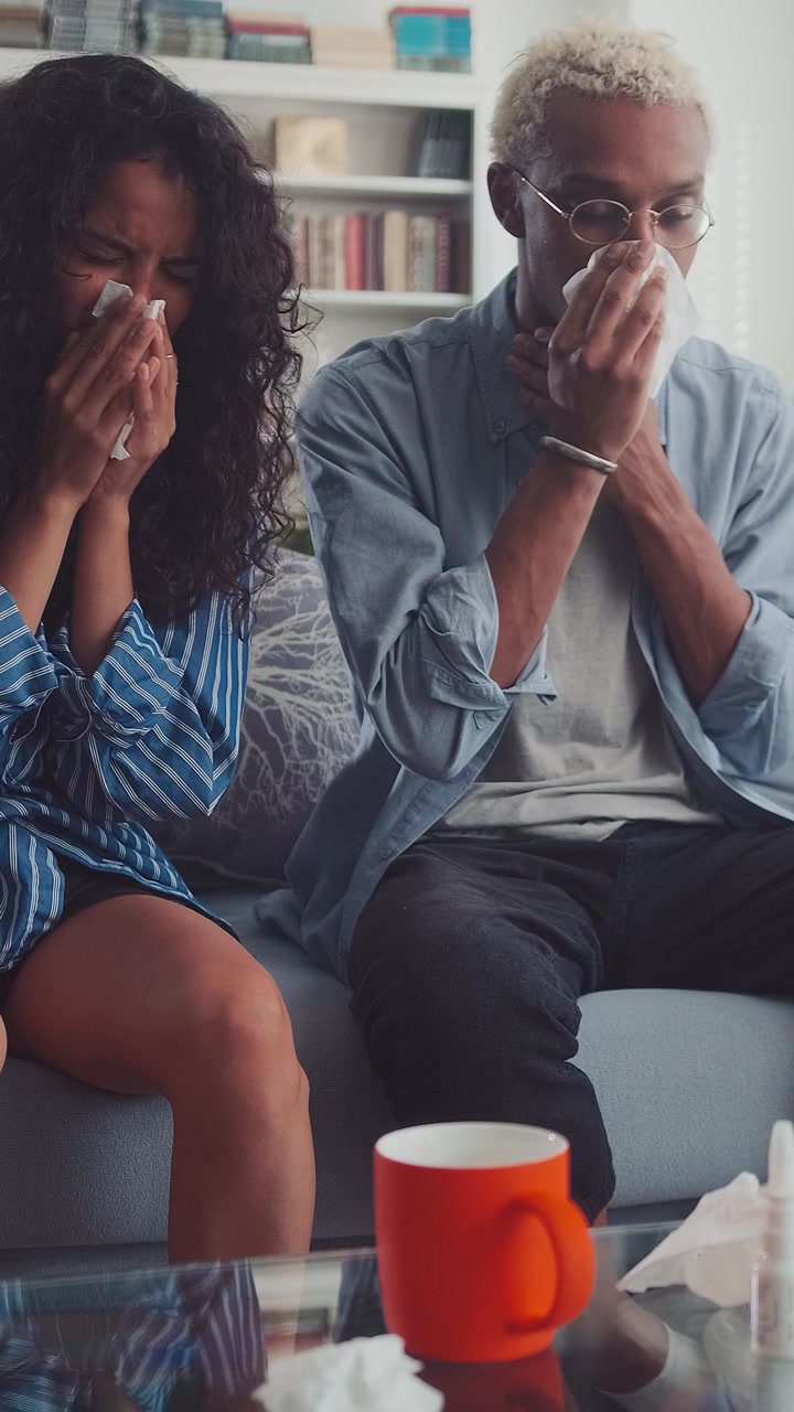 Homme afro-américain et femme indienne malades se mouchant sur le canapé