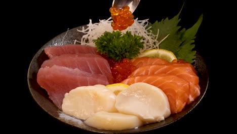 assorted sashimi and sushi, including salmon, tuna, scallop, and roe, elegantly arranged on a plate, rotating under studio lighting against a black background