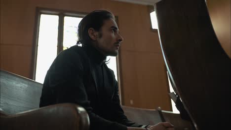 young man in black suit praying in church pew in cinematic slow motion with folded hands