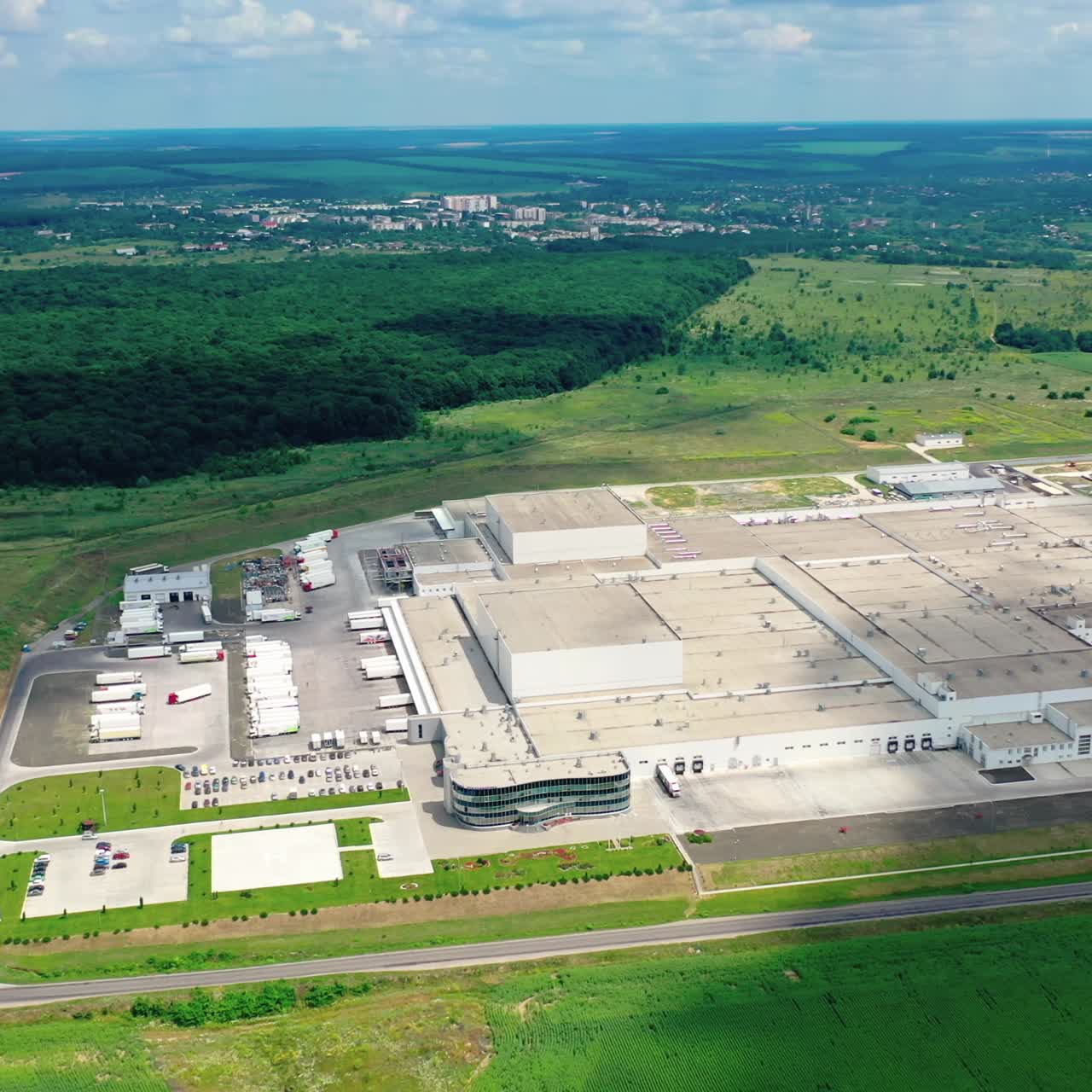 Roofs of a huge industrial plant at sunlight. Modern factory of white building with places for cars and trucks on green field