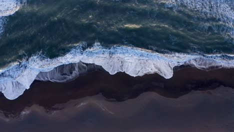 vista de las olas del océano de la costa sur que lavan la playa de arena basáltica negra - drone aéreo