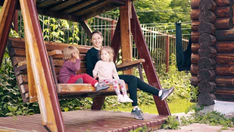 Travelling-Young-pretty-mother-with-children-swinging-on-a-wooden-swing-near-the-summer-house-3