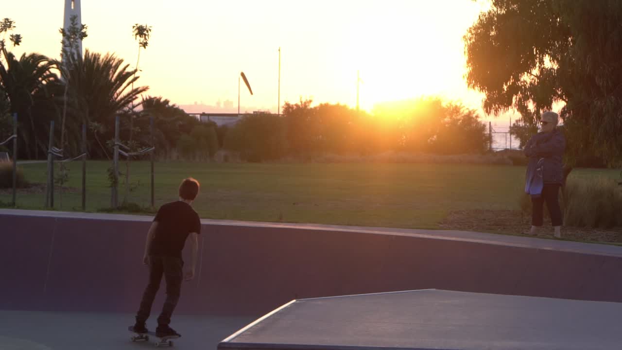 Ripresa al rallentatore di un ragazzo che scende in pista in uno skate park al tramonto.