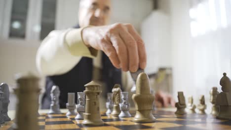 Happy retired man plays chess alone at home.