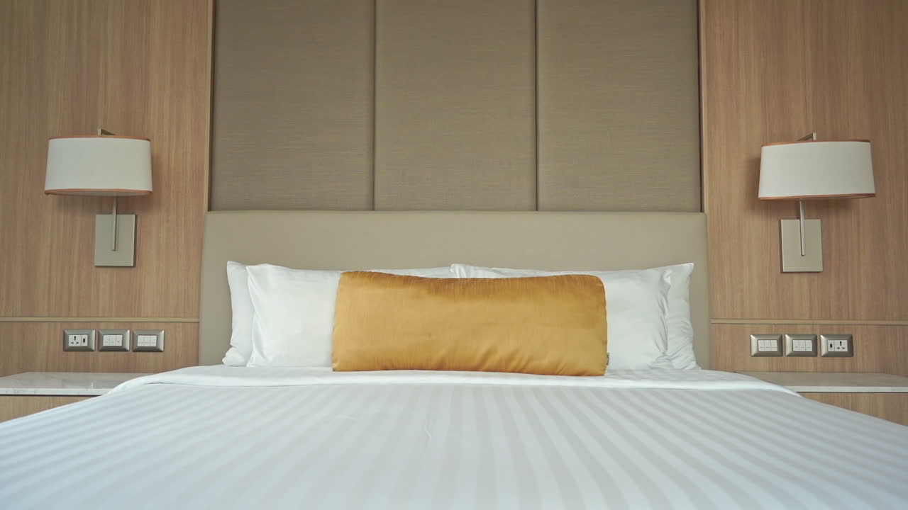 Pan from headboard to foot of the bed, a golden pillow sitting on top of a resort hotel room bed welcoming visitors