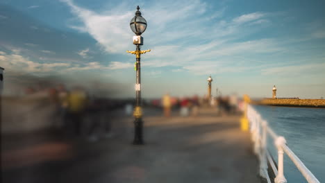 Whitby-Pier-Timelapse,-Blurred-crowds-in-the-summer-evening-sun,-Whitby-harbour-entrance,-North-Yorkshire