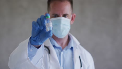 médico caucásico con máscara facial y vacuna en la mano